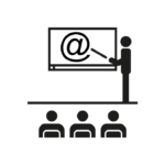 Una silueta señala con un puntero en una pantalla que tiene una arroba. Está ante un grupo de personas
