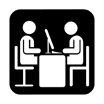 Una persona sentada en una mesa con ordenador atiende a otra que también está sentada